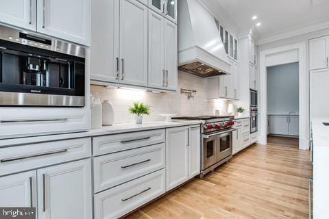 kitchen with white cabinetry, tasteful backsplash, premium range hood, crown molding, and double oven range