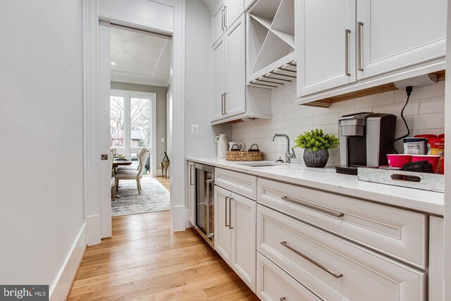 kitchen featuring light stone countertops, beverage cooler, sink, white cabinets, and light hardwood / wood-style floors