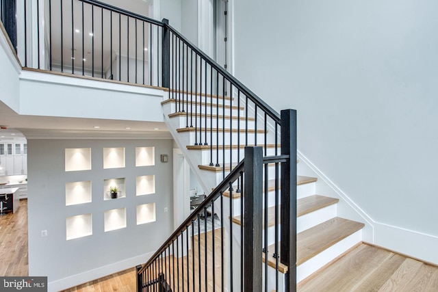 staircase with wood-type flooring, ornamental molding, and a towering ceiling