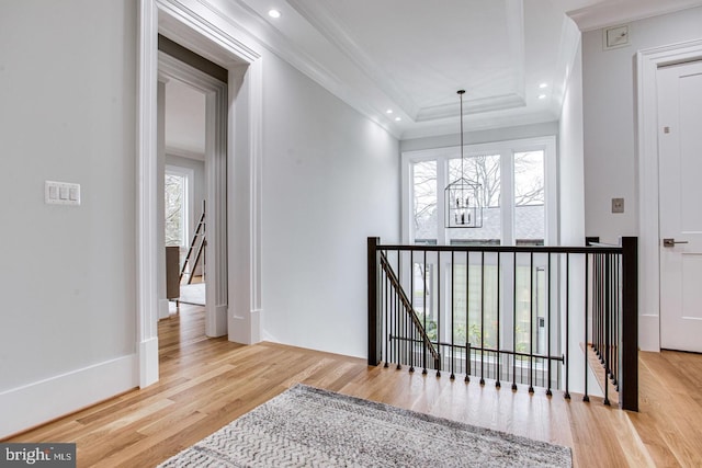 corridor featuring a tray ceiling, light hardwood / wood-style flooring, plenty of natural light, and crown molding