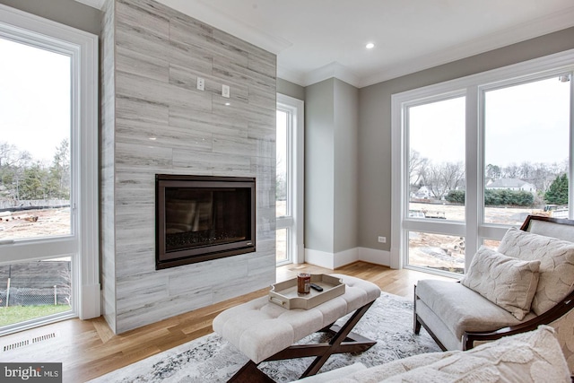 living room with light hardwood / wood-style floors, plenty of natural light, crown molding, and a tiled fireplace