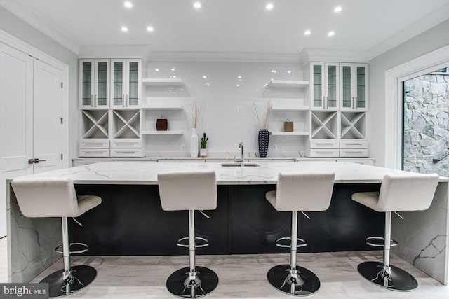 bar featuring sink, light stone counters, white cabinetry, and crown molding