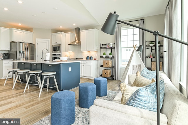 kitchen featuring wall chimney range hood, white cabinetry, stainless steel appliances, and an island with sink