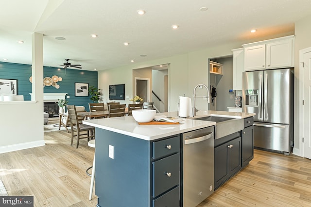 kitchen with an island with sink, ceiling fan, stainless steel appliances, light hardwood / wood-style flooring, and white cabinets