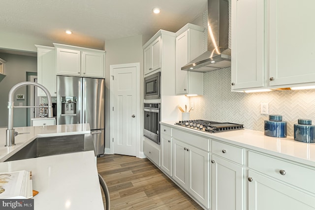 kitchen with white cabinetry, appliances with stainless steel finishes, light wood-type flooring, tasteful backsplash, and wall chimney exhaust hood