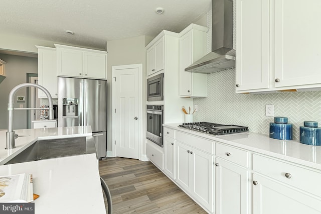 kitchen with white cabinets, light hardwood / wood-style floors, stainless steel appliances, wall chimney exhaust hood, and tasteful backsplash