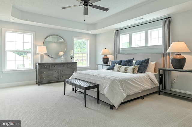 bedroom with ceiling fan, light colored carpet, and a tray ceiling