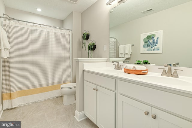 bathroom with dual sinks, tile flooring, a textured ceiling, vanity with extensive cabinet space, and toilet