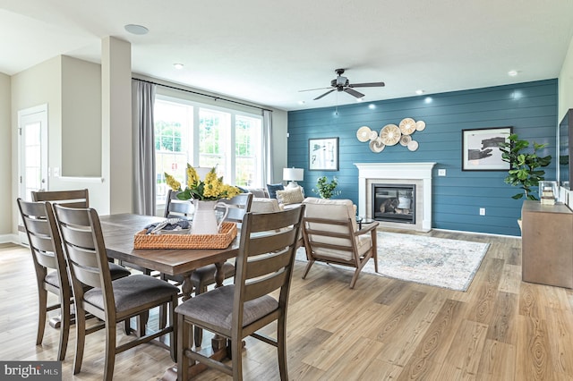 dining room featuring ceiling fan, light wood-type flooring, and wooden walls