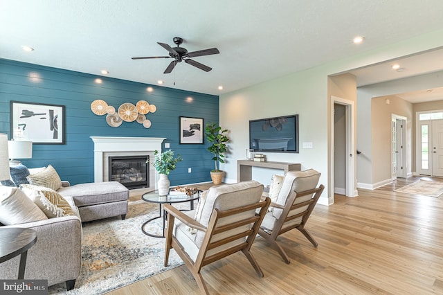 living room with wood walls, ceiling fan, and light wood-type flooring