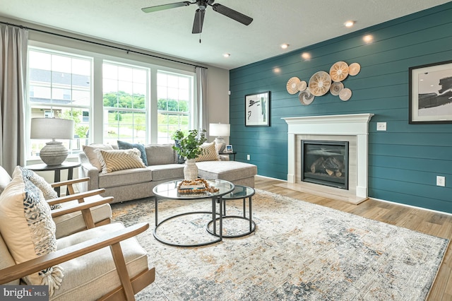 living room with ceiling fan, wood walls, and light wood-type flooring