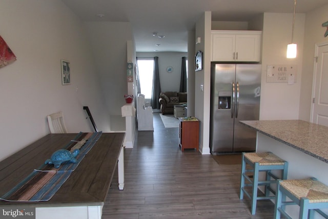 kitchen featuring dark hardwood / wood-style floors, stainless steel fridge, hanging light fixtures, a breakfast bar, and white cabinetry