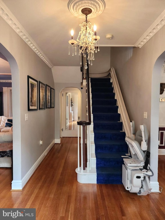 staircase featuring crown molding, wood-type flooring, and a notable chandelier