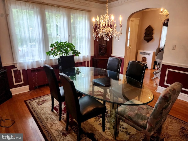 dining room with radiator heating unit, a notable chandelier, hardwood / wood-style flooring, and ornamental molding