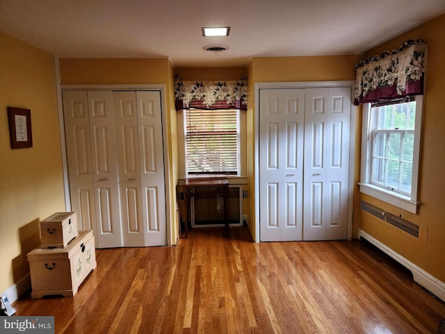 unfurnished bedroom with two closets, hardwood / wood-style flooring, and radiator