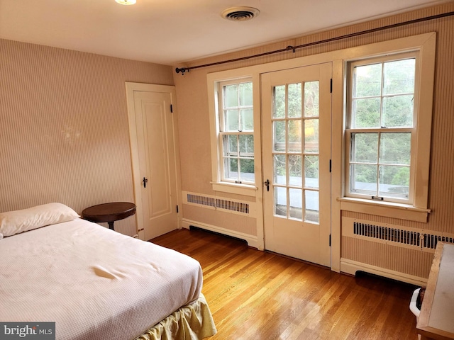 bedroom featuring multiple windows, hardwood / wood-style floors, and radiator heating unit