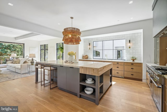 kitchen with beam ceiling, wall chimney range hood, a kitchen island, decorative backsplash, and high end range