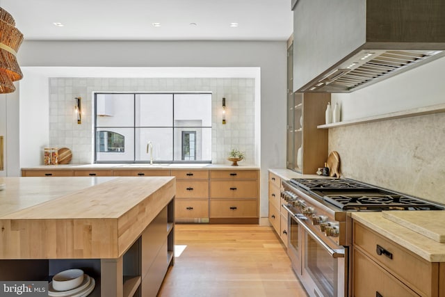 kitchen with wall chimney exhaust hood, wood counters, decorative backsplash, high end stainless steel range, and light wood-type flooring