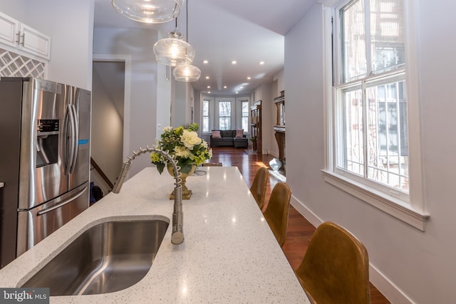 kitchen featuring hanging light fixtures, stainless steel fridge, dark hardwood / wood-style flooring, light stone countertops, and white cabinets