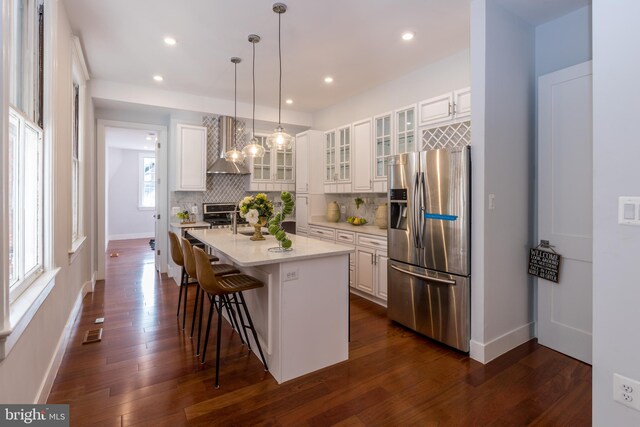 kitchen featuring dark hardwood / wood-style floors, white cabinetry, wall chimney exhaust hood, and stainless steel fridge