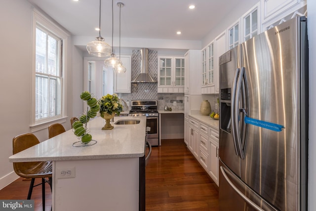 kitchen featuring wall chimney range hood, a breakfast bar area, white cabinets, and appliances with stainless steel finishes