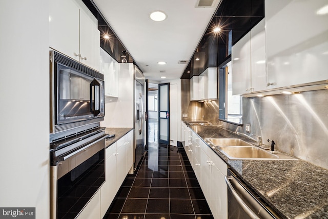 kitchen with backsplash, appliances with stainless steel finishes, dark tile floors, sink, and dark stone countertops