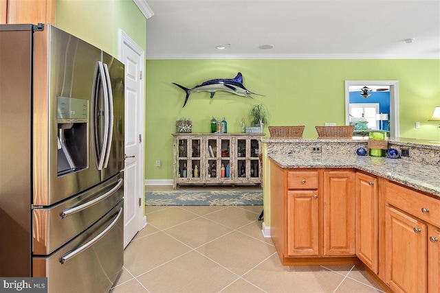 kitchen with crown molding, light stone counters, light tile floors, and stainless steel fridge