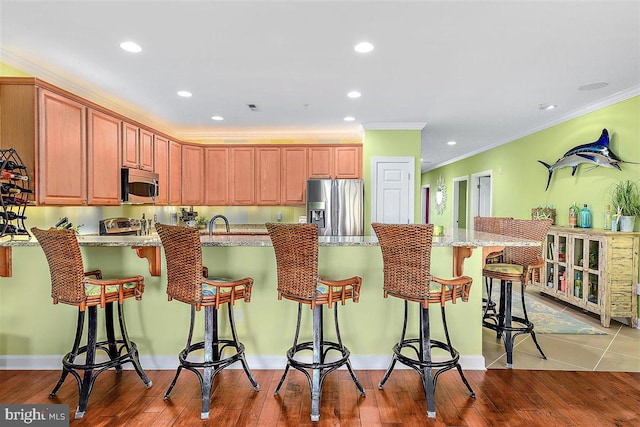 kitchen featuring a kitchen breakfast bar, ornamental molding, a center island with sink, stainless steel appliances, and light stone countertops