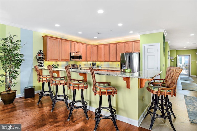 kitchen with appliances with stainless steel finishes, a breakfast bar, light hardwood / wood-style flooring, light stone countertops, and ornamental molding