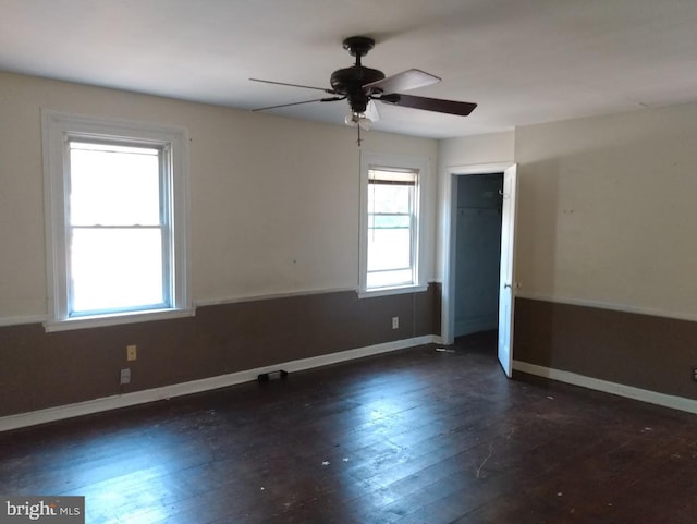 empty room featuring ceiling fan, dark wood-type flooring, and a wealth of natural light