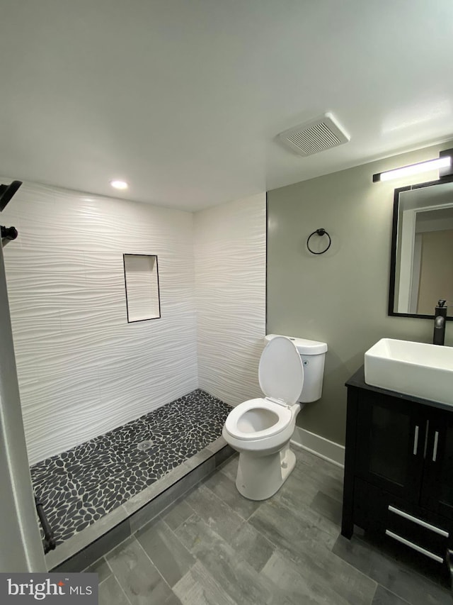 bathroom with a tile shower, vanity, and toilet