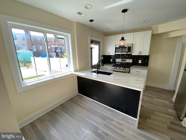 kitchen with white cabinetry, sink, stainless steel appliances, light stone counters, and kitchen peninsula