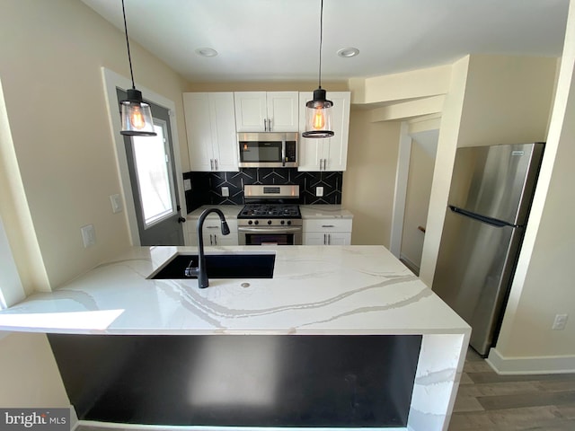 kitchen featuring kitchen peninsula, appliances with stainless steel finishes, tasteful backsplash, decorative light fixtures, and white cabinetry