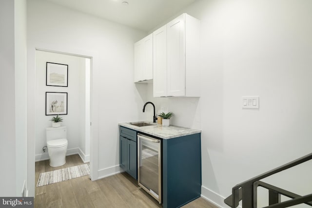 interior space featuring sink, white cabinets, light stone countertops, wine cooler, and light wood-type flooring