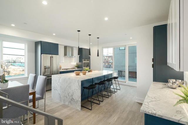 kitchen with hanging light fixtures, appliances with stainless steel finishes, light stone counters, and plenty of natural light