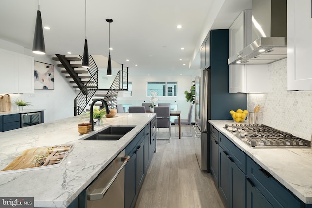 kitchen featuring hanging light fixtures, light hardwood / wood-style floors, white cabinets, light stone counters, and wall chimney range hood