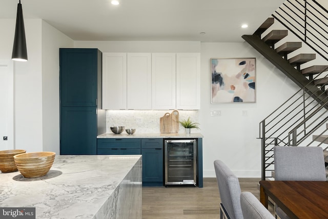 kitchen with white cabinets, beverage cooler, hardwood / wood-style floors, light stone countertops, and backsplash