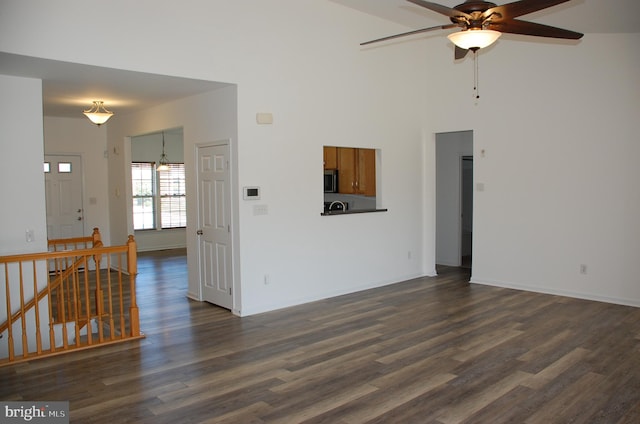 living room with dark hardwood / wood-style flooring, ceiling fan with notable chandelier, and a high ceiling