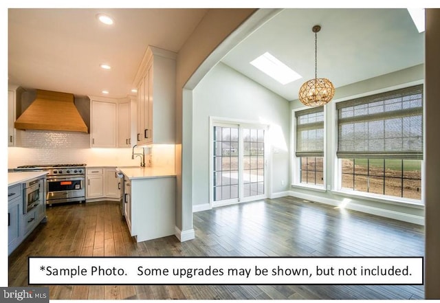 kitchen featuring vaulted ceiling with skylight, appliances with stainless steel finishes, white cabinetry, hanging light fixtures, and custom range hood