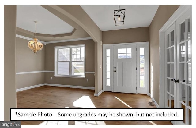 foyer with hardwood / wood-style floors, ornamental molding, a raised ceiling, and an inviting chandelier