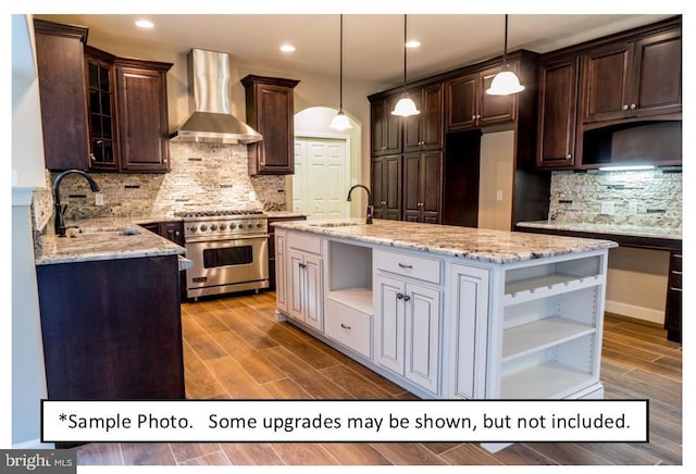 kitchen with high end stainless steel range, sink, wall chimney range hood, and decorative light fixtures