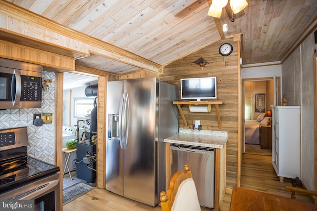 kitchen featuring wood walls, light hardwood / wood-style floors, ceiling fan, appliances with stainless steel finishes, and lofted ceiling