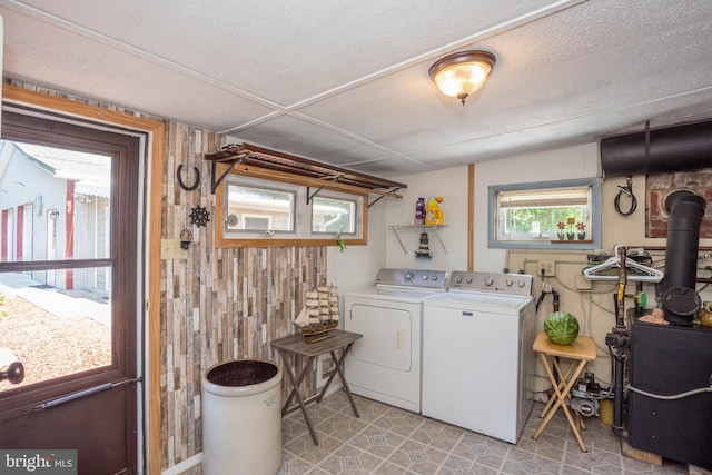 washroom with a wood stove, light tile flooring, a textured ceiling, separate washer and dryer, and wooden walls