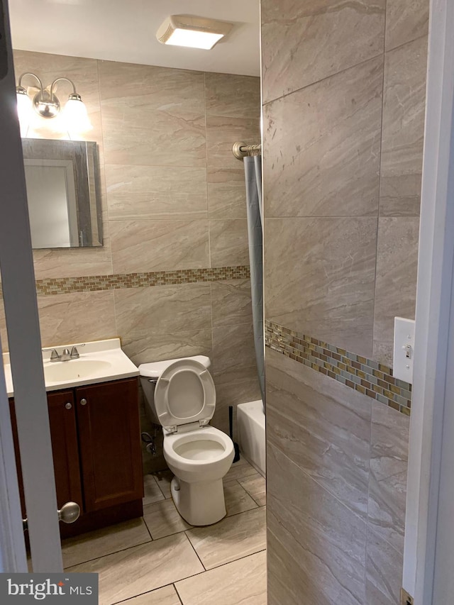 full bathroom with tile walls, toilet, tiled shower / bath, tile flooring, and large vanity