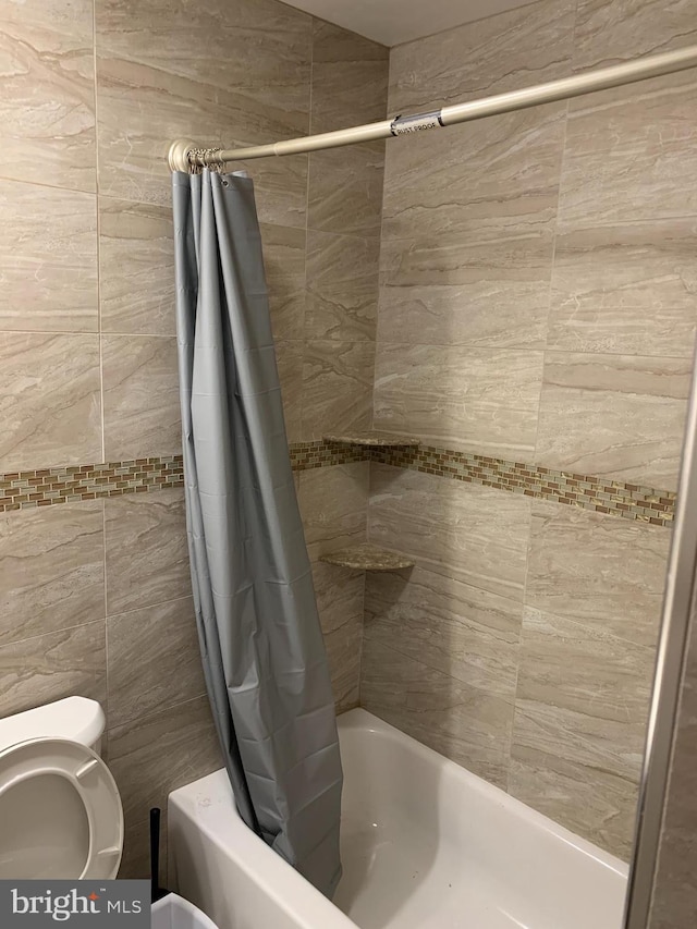 bathroom featuring tile walls, toilet, and shower / bathtub combination with curtain