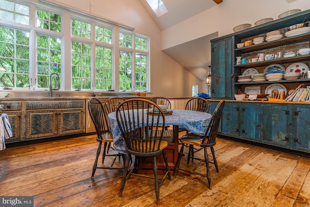 dining room with vaulted ceiling with skylight, light wood-type flooring, and sink