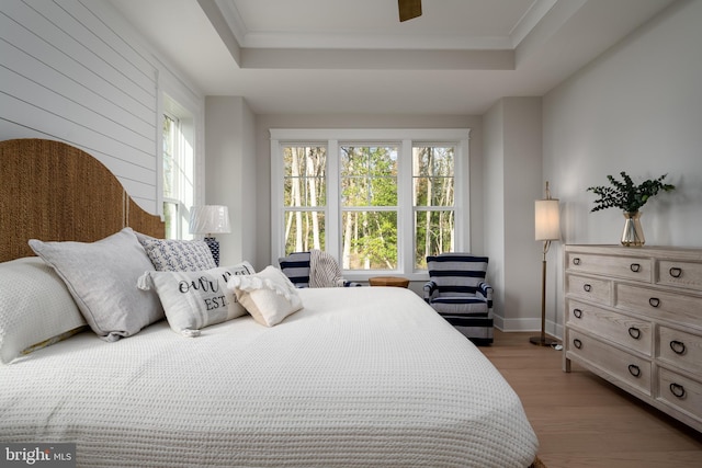 bedroom featuring a tray ceiling, ceiling fan, crown molding, and light hardwood / wood-style flooring