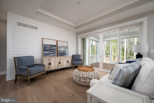 living room with wood walls, wood-type flooring, and a tray ceiling