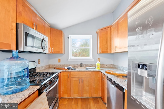 kitchen with vaulted ceiling, light stone counters, stainless steel appliances, light hardwood / wood-style flooring, and sink