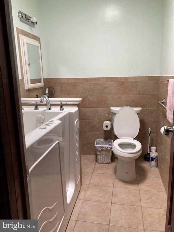 bathroom with tile walls, toilet, and tile floors